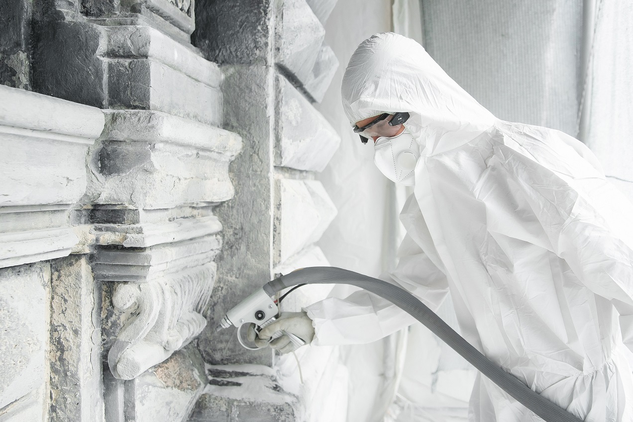 Man in a white protective uniform cleans stone carved sculpture from the dirt and concrete with a sandblasting machine. Restoration of stone sculpture. A jet of sand under high pressure.